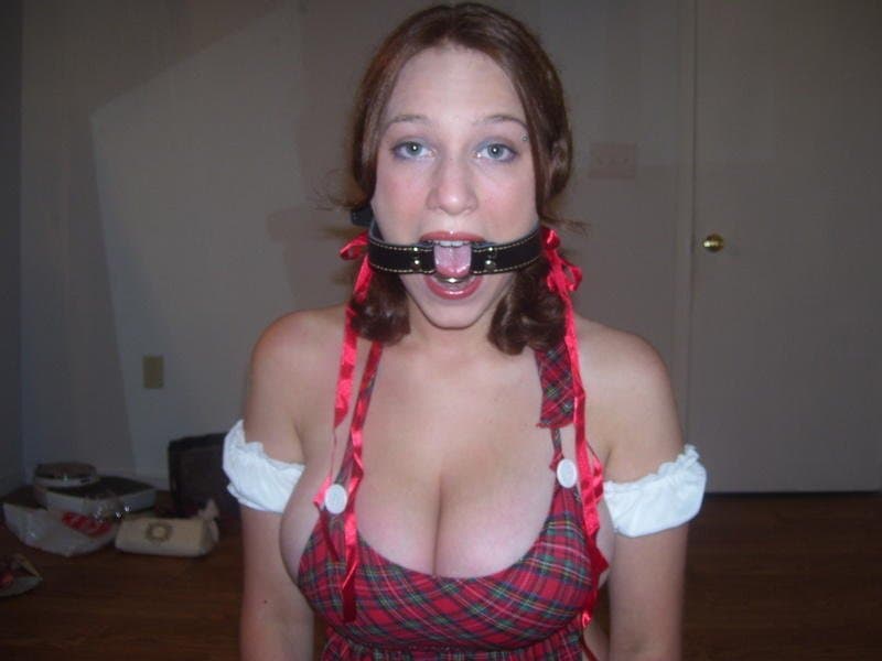 Submissive Redhead with massive jugs poses with her ball gag